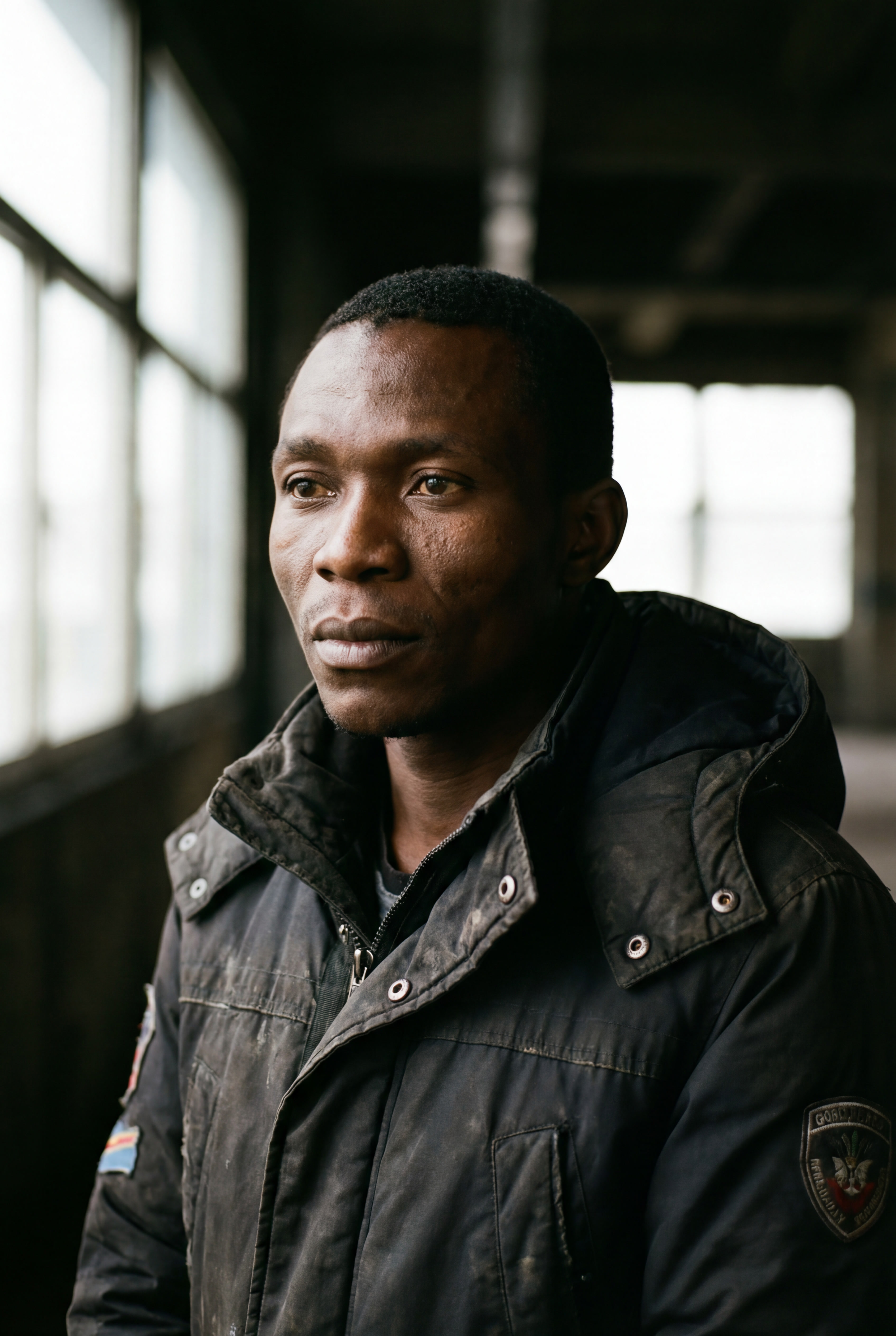Joseph Kabongo, a young Congolese man, in a worn winter jacket, lit by a window.