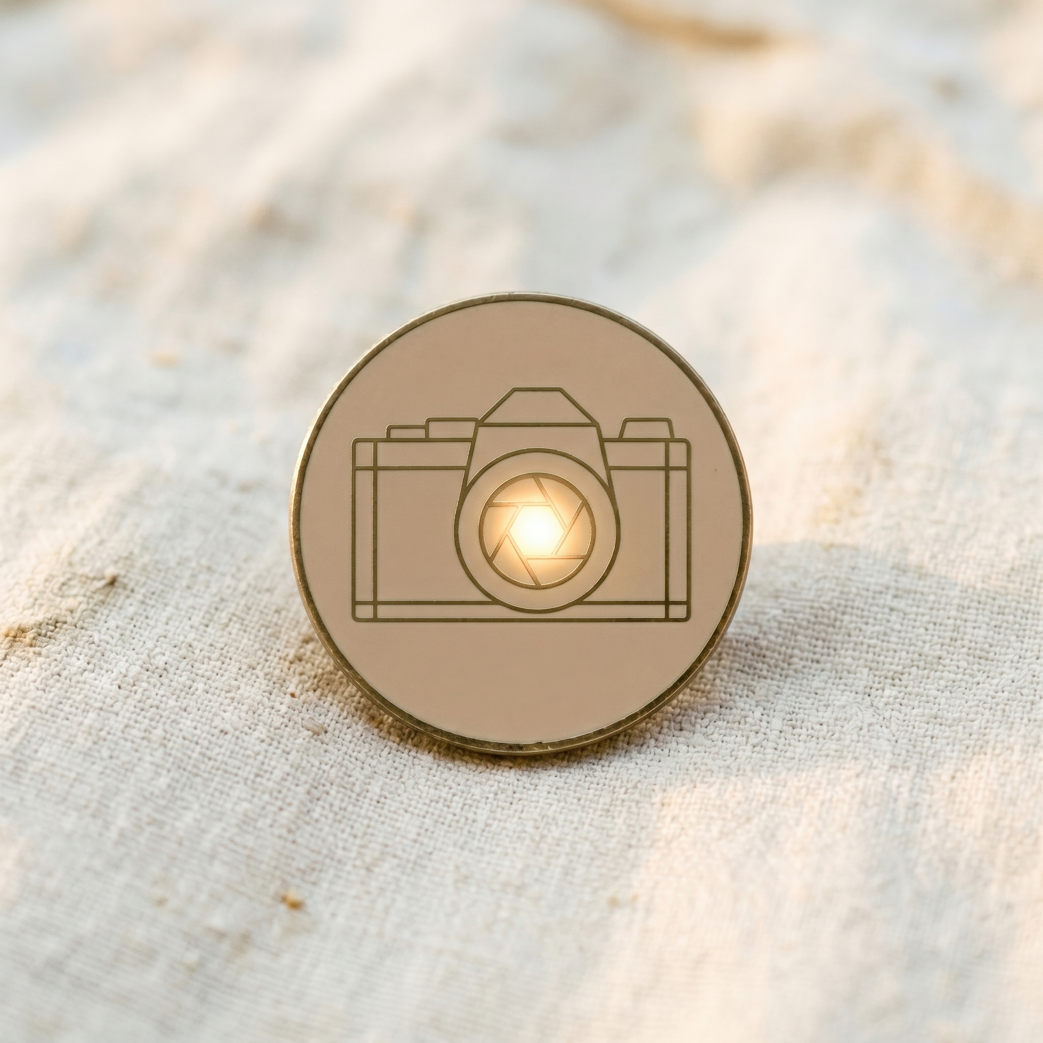 A minimalist round enamel pin - a geometric line-art vintage SLR camera with a glowing lens.